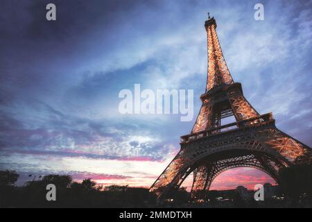 Les lumières s'allument dans la Tour Eiffel tandis que le soleil s'estompe sous l'horizon. Banque D'Images