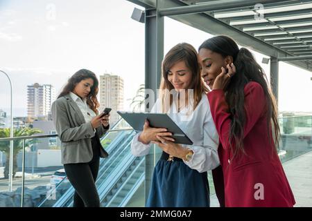 Deux femmes d'affaires consultent leur tablette tandis qu'une autre regarde son smartphone en arrière-plan Banque D'Images