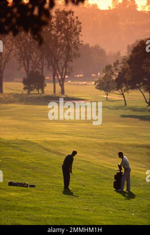 Vue longue de deux hommes sur le parcours de golf lorsque le soleil commence à se coucher Banque D'Images