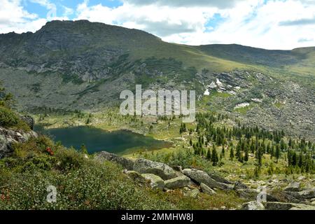 Une vue du sommet d'une montagne rocheuse à un petit lac allongé dans un creux entouré de montagnes par un ciel nuageux jour d'été. Parc naturel Ergaki, Krasnoy Banque D'Images