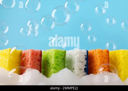 Nettoyage ménager nettoyer les éponges colorées avec de la mousse de savon et des bulles. Éponge pour lave-vaisselle de cuisine sur fond bleu. Concept de ménage. Espace pour t Banque D'Images