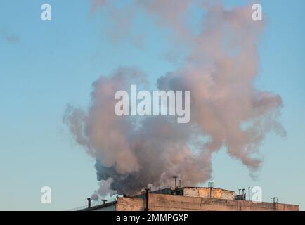 Cheminée en briques avec fumée blanche sur un bâtiment industriel. Banque D'Images