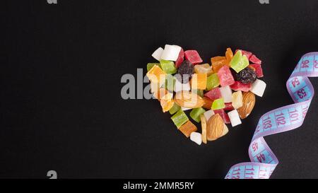 Concept alimentaire pour la Saint-Valentin. Concept amincissant. Fruits secs et noix en forme de coeur et ruban de mesure isolé sur fond noir, copie de spac Banque D'Images