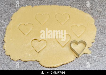 Fabrication de biscuits faits maison en forme de coeur. Pâte avec emporte-pièces cuits et emporte-pièces en forme de cœur sur une table de cuisine à tendance grise, vue du dessus. Su Banque D'Images