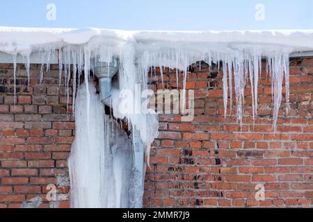 De longues glaces transparentes pendent du toit. La gouttière glacée est comme une glace géante. Icicles tombant danger concept. Banque D'Images