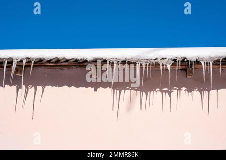 Très belles glaces suspendues au toit recouvert de neige. Icicles tombant danger concept. Banque D'Images