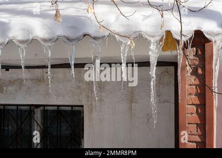 De longues glaces pendent du toit enneigé d'une ancienne maison rose. Icicles tombant danger concept. Banque D'Images