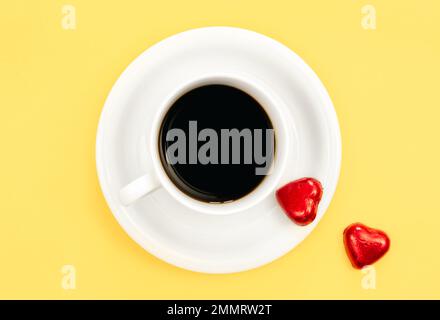 Une tasse de café et de bonbons en forme de coeur sur fond jaune, plat. Banque D'Images