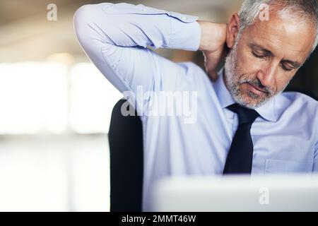 Trop d'heures devant l'ordinateur... un homme d'affaires mûr qui semble stressé pendant qu'il travaille dans son bureau. Banque D'Images