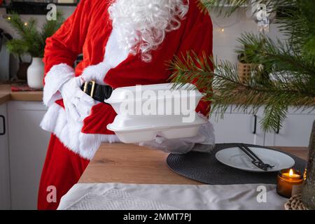 Livraison de nourriture à domicile conteneurs de service dans les mains du Père Noël le met sur la table de cuisine et le prend loin. Commande à chaud prête à l'emploi, Noël, nouvel an Banque D'Images