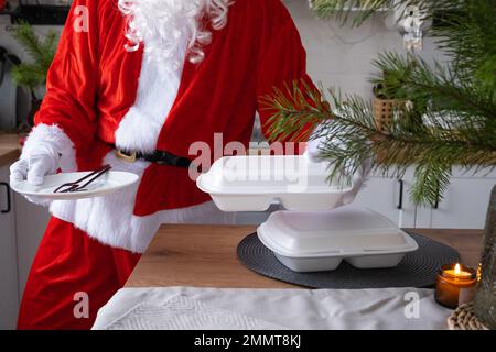 Livraison de nourriture à domicile conteneurs de service dans les mains du Père Noël le met sur la table de cuisine et le prend loin. Commande à chaud prête à l'emploi, Noël, nouvel an Banque D'Images