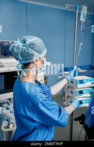 Infirmier en chirurgie portant un uniforme de protection préparant le compte-gouttes médical pour le patient en salle d'opération Banque D'Images