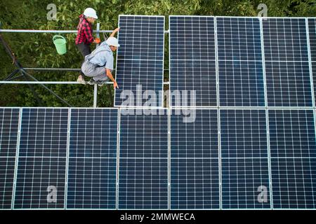 Deux hommes en casques de sécurité installant un panneau solaire photovoltaïque. Techniciens mâles plaçant le module solaire sur la structure de support lors de l'assemblage du système de panneaux photovoltaïques solaires. Banque D'Images