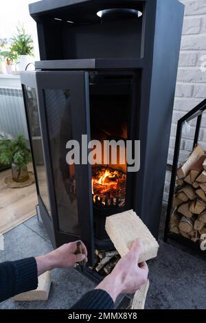 Les mains kindle le foyer avec des briquettes économiques. Briquettes de combustible en sciure pressée pour l'allumage du four - alternative économique éco-frie Banque D'Images