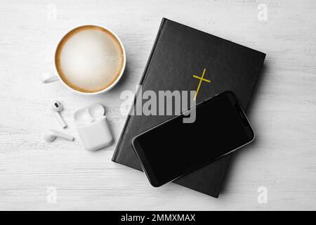 Bible, téléphone, tasse de café et écouteurs sur fond blanc en bois, plat. Livre audio religieux Banque D'Images