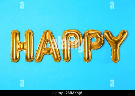 Mot HEUREUX fait de lettres de ballon d'aluminium doré sur fond bleu clair Banque D'Images