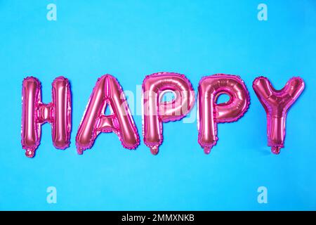 Mot HEUREUX fait de lettres de ballon de feuille rose sur fond bleu clair Banque D'Images