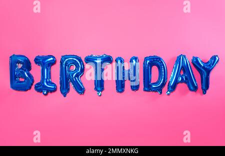Anniversaire mot fait de lettres de ballon d'aluminium bleu sur fond rose Banque D'Images