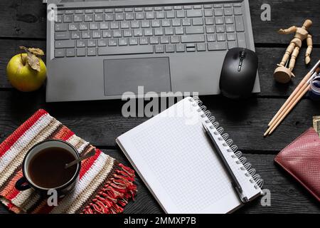 un bloc-notes noir pour ordinateur portable avec de l'argent pour le café se trouve sur la table de travail en bois noir, un ordinateur portable sur la table de travail pendant le travail, processus créatif, indépendant Banque D'Images