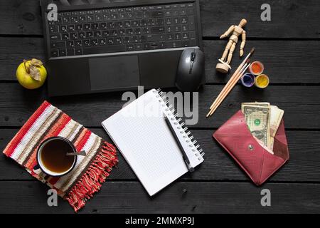 un bloc-notes noir pour ordinateur portable avec de l'argent pour le café se trouve sur la table de travail en bois noir, un ordinateur portable sur la table de travail pendant le travail, processus créatif, indépendant Banque D'Images