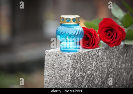 Roses rouges et bougie sur pierre tombale de granit gris à l'extérieur. Cérémonie funéraire Banque D'Images