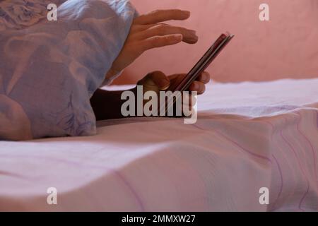 une fille tient un téléphone dans ses mains sur le lit la nuit dans la chambre à coucher, la communication sur le téléphone tout en dormant la nuit sur le lit, un téléphone dans sa ha Banque D'Images