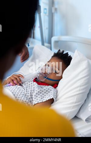 Enfant afro-américain dans un masque respiratoire d'hôpital, regardant vers la mère avec un espace de copie Banque D'Images