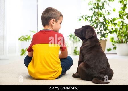 Petit garçon avec un chiot sur le sol à la maison. Chien sympathique Banque D'Images