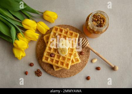 Gaufres belges faites maison avec miel, noix et tulipes jaunes. nature morte avec tulipes. Banque D'Images