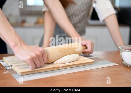 Gros plan d'un homme pétriant de la pâte avec une broche roulante, aidant sa petite amie à cuire de la pâte dans la cuisine. Banque D'Images