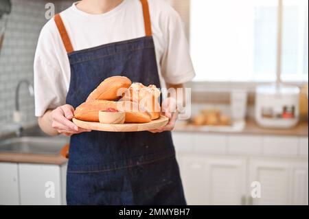 Image rognée d'un jeune asiatique en tablier tenant un plateau de pâte fraîche dans sa cuisine. concept de cuisson à la maison Banque D'Images