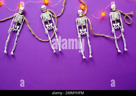 Halloween mise en page d'une guirlande de squelettes sur une corde, lueur Jack o Lantern, citrouilles sur un fond violet. Flat Lay horreur et des vacances terribles Banque D'Images