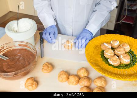 Préparation de profiteroles à la crème et au chocolat. La personne avec des ingrédients remplit les choux vides de crème fouettée Banque D'Images