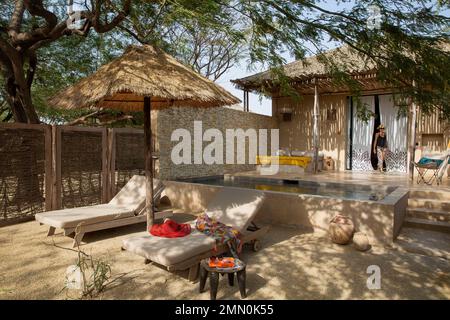 Sénégal, delta de Saloum classé au patrimoine mondial par l'UNESCO, Palmarin, Yokan Lodge, femme sortant de sa suite prolongée par une terrasse accueillant une piscine privée et des parasols à l'ombre d'un arbre tentaculaire Banque D'Images