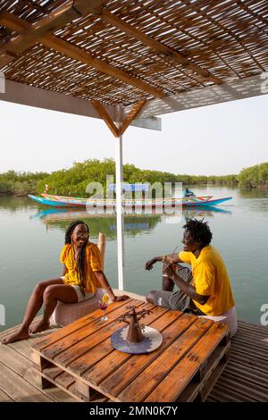 Sénégal, delta de Saloum classé au patrimoine mondial par l'UNESCO, couple de jeunes Sénégalais ayant un verre sur la plate-forme flottante de l'agence de tourisme les Aventuriers du Saloum au milieu de la mangrove Banque D'Images