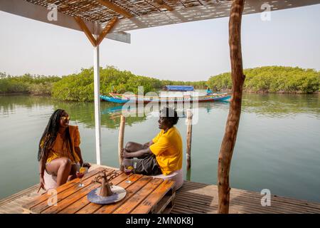 Sénégal, delta de Saloum classé au patrimoine mondial par l'UNESCO, couple de jeunes Sénégalais ayant un verre sur la plate-forme flottante de l'agence de tourisme les Aventuriers du Saloum au milieu de la mangrove Banque D'Images