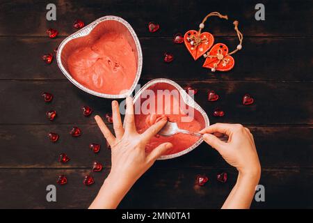 La femme enlève la pâte de la cuillère avec son doigt, le processus de faire un gâteau sous forme de coeur. Préparation pour la Saint-Valentin. Banque D'Images