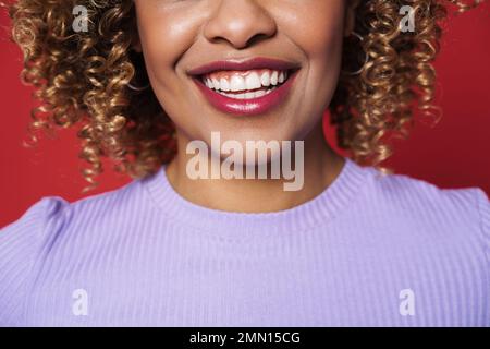 Portrait court de belle jeune femme bouclé souriante avec des lèvres rouges sur un arrière-plan rouge isolé Banque D'Images