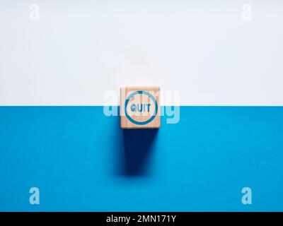 Le mot Quitter sur bouton-poussoir cube en bois sur fond bleu et blanc. Décision de quitter un emploi ou de fumer concept. Banque D'Images