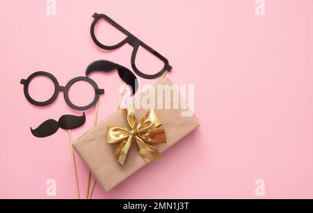 Vue à plat du cadeau de Père emballé avec moustache et lunettes sur fond rose, beaucoup d'espace de copie. Maquette de carte de vœux amusante. Banque D'Images