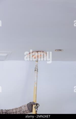 Le travailleur a poncé la boue de cloisons sèches à l'aide d'une truelle de sable au moment de la rénovation de la maison dans la pièce Banque D'Images