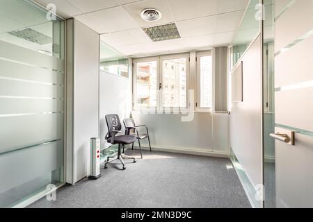 Intérieur d'un couloir blanc-gris dans un style simple et de bureau. Deux bureaux, à gauche et à droite, avec des cloisons en verre et entre eux, petits, éclairés au soleil Banque D'Images