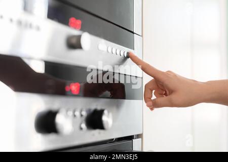 Une main féminine touche le bandeau de commande du four électrique dans la cuisine Banque D'Images