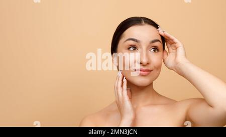 Publicité beauté. Belle jeune femme indienne souriante touchant le visage et regardant loin Banque D'Images