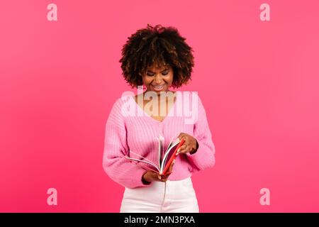 Souriant élégant jeune afro-américaine curly dame étudiant dans un livre de lecture décontracté, journal Banque D'Images