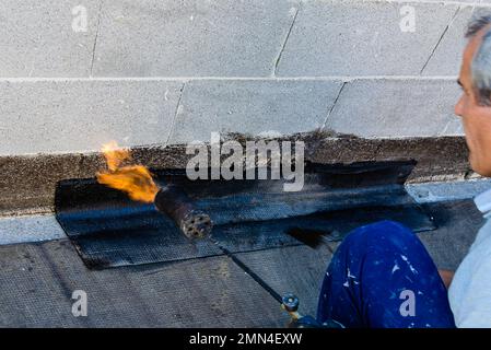 Chalumeau au propane au travail d'isolation de la dalle de plancher. Le revêtement de toit plat fonctionne avec du feutre de toiture Banque D'Images