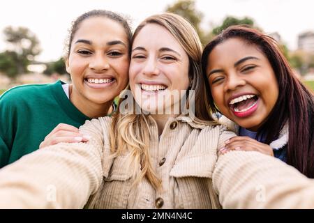 Jeune groupe de trois femmes gaies diverses prenant le selfie ensemble à l'extérieur Banque D'Images