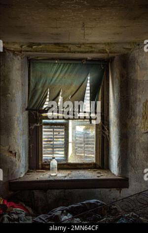 Fenêtre cassée, rideaux déchirés et bouteille sale dans l'intérieur de maison abandonnée, Pennsylvanie USA Banque D'Images