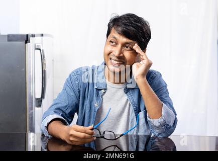 Un mâle indien avec des lunettes face au mal de tête assis à côté d'une table sur fond blanc Banque D'Images