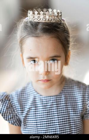 Une fille en robe à carreaux et une couronne sourit et est triste. La princesse pose strictement. Photo de haute qualité Banque D'Images